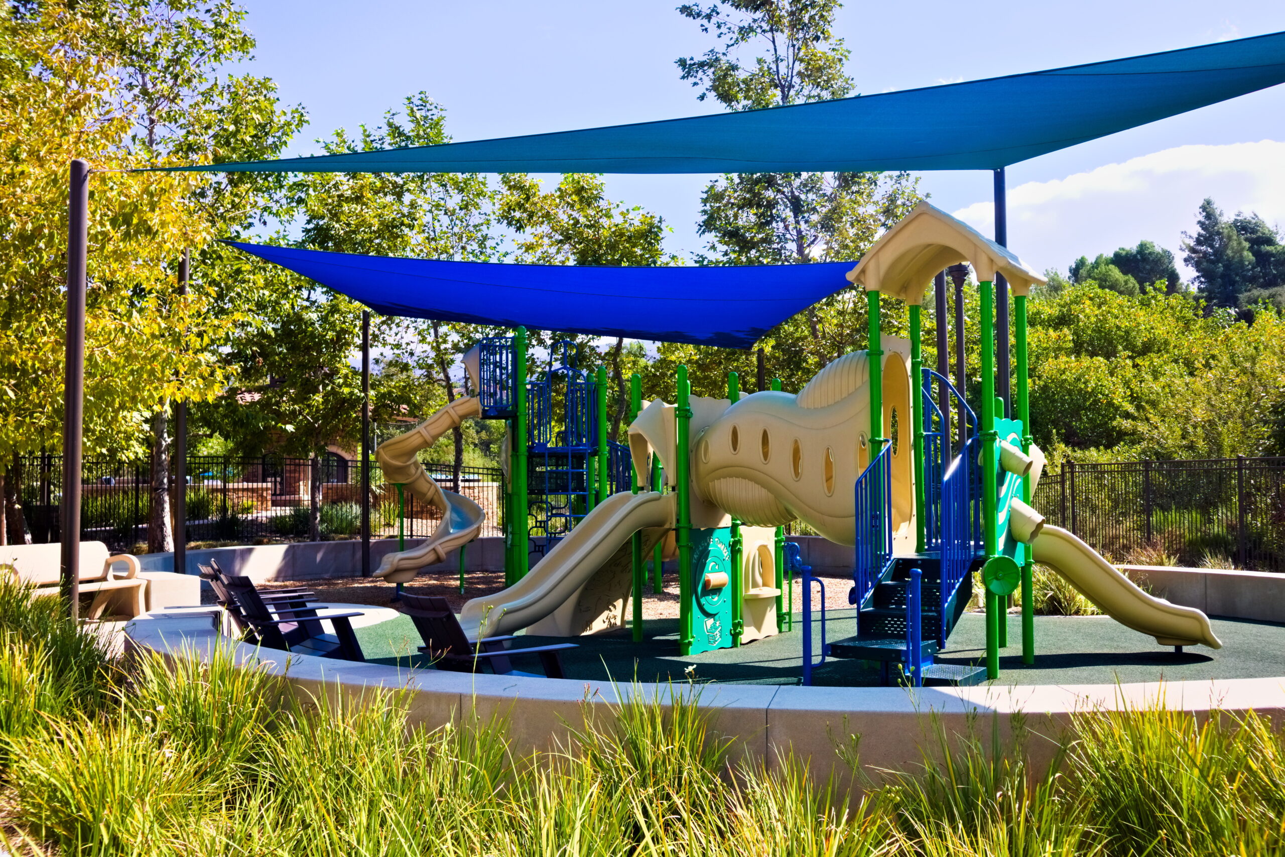 Colorful playground featuring slides, shade covers, and play structures surrounded by trees.