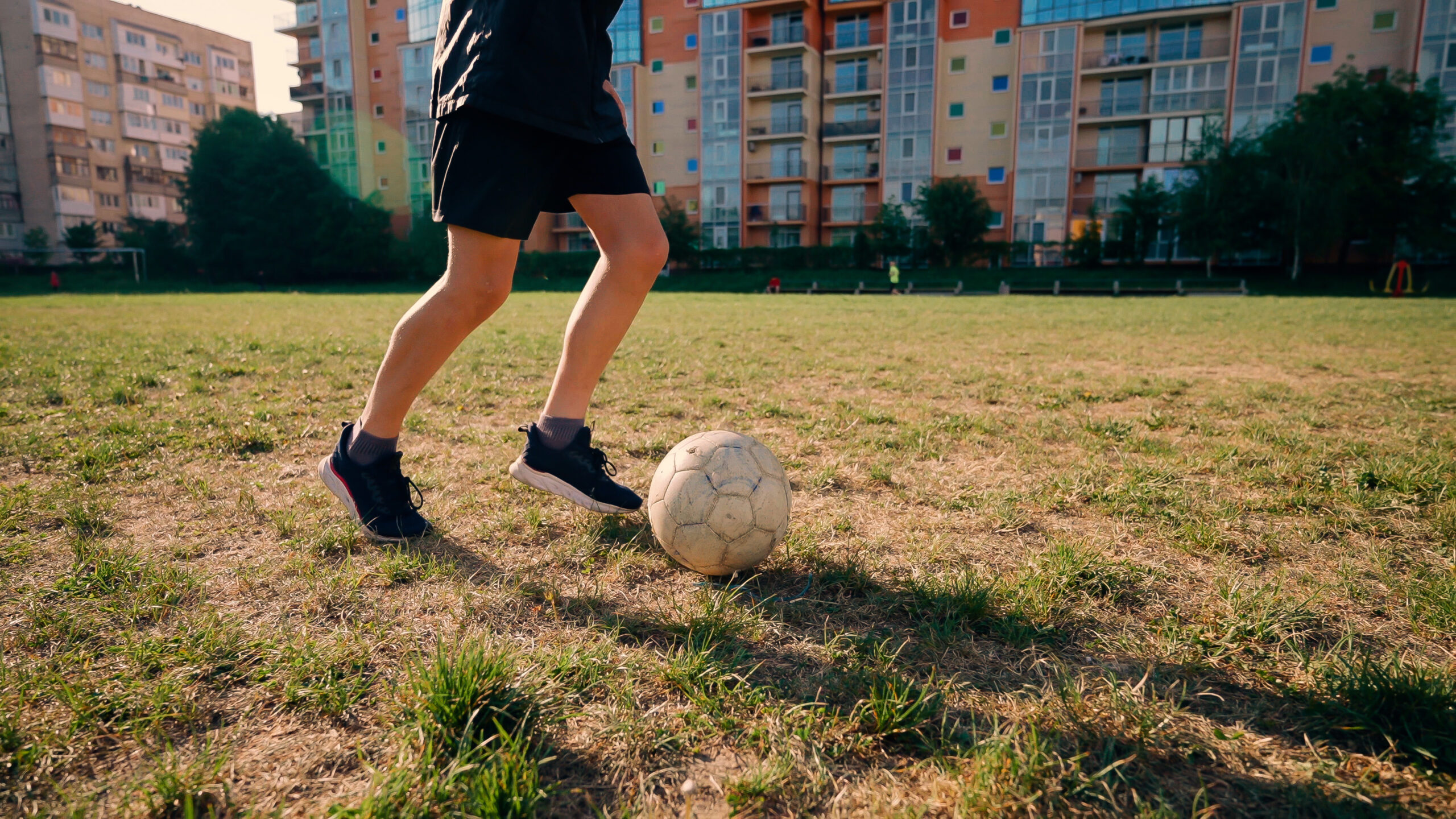 A young athlete trains and runs forward and kicks ball. Soccer player on green grass practices driving ball.