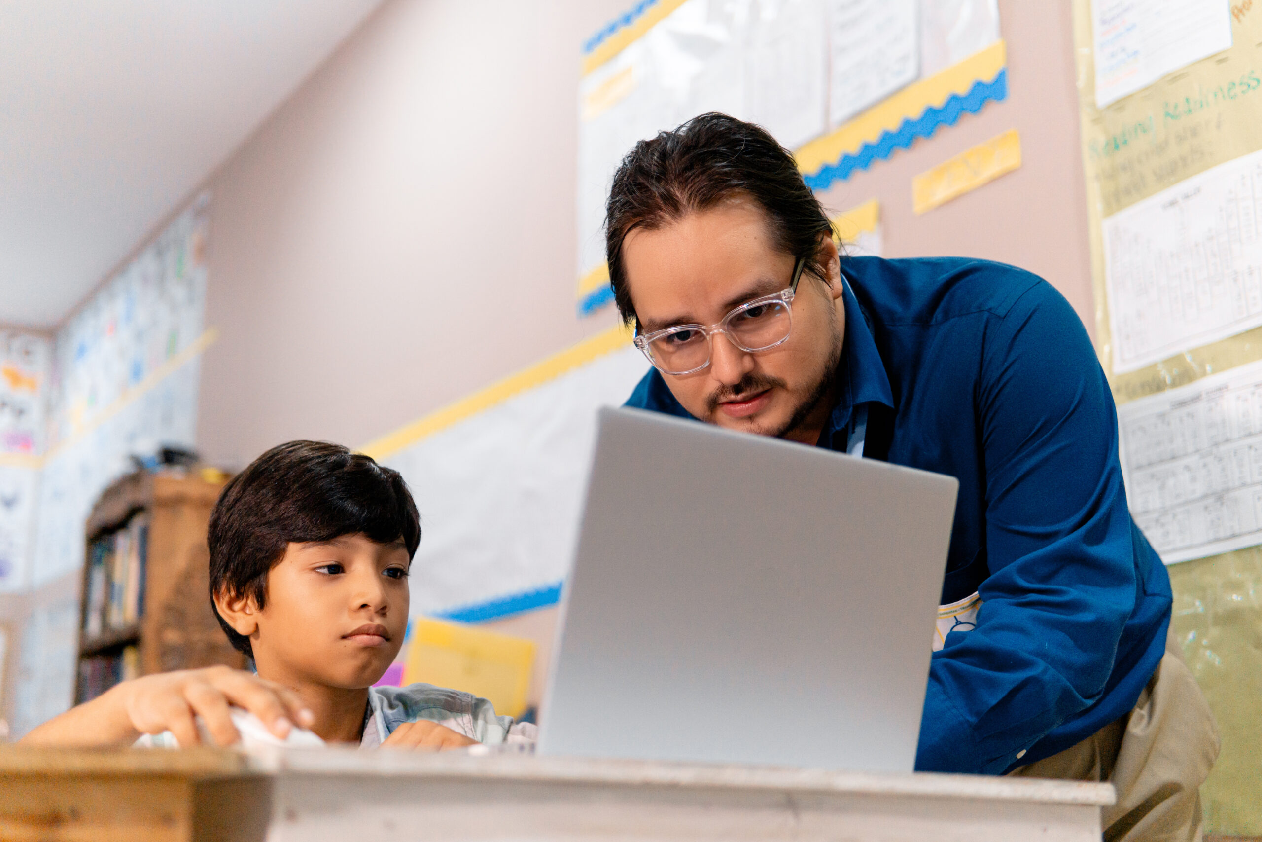 male teacher and schoolboy using laptop in elementary school class