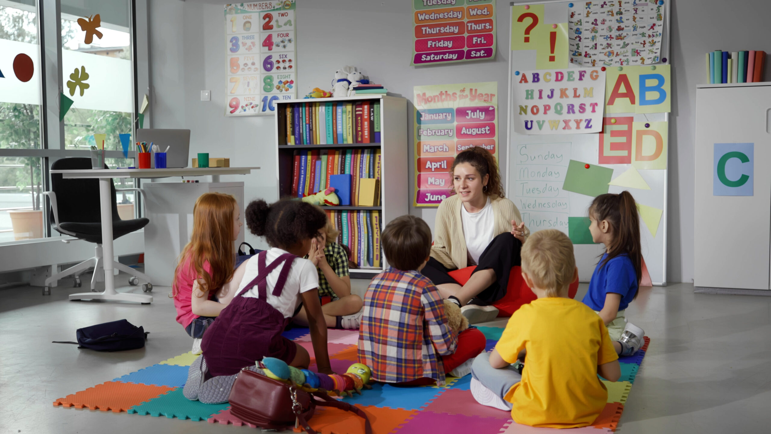 Small nursery school children with teacher sitting on floor having lesson.