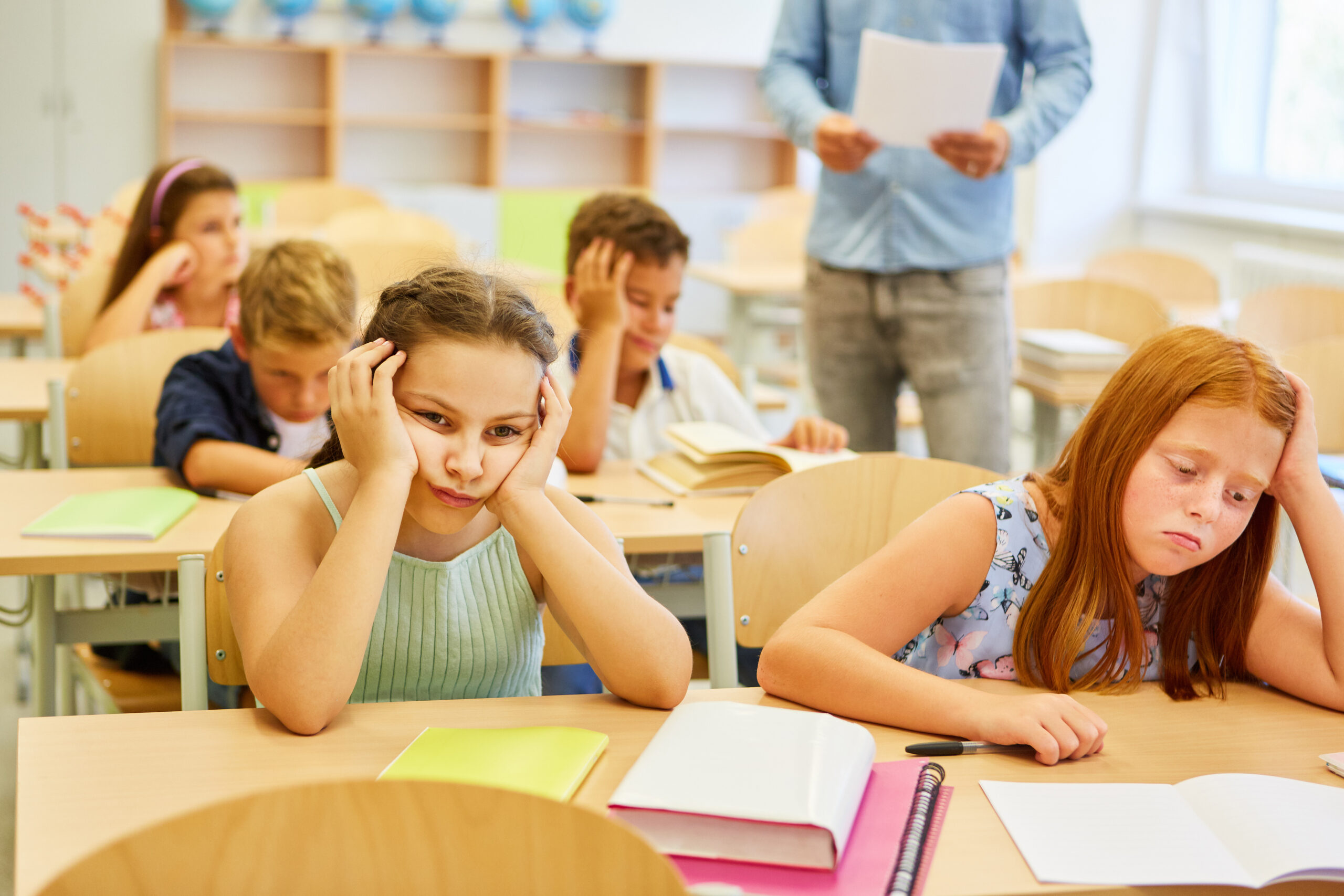 Tired female friends sitting on bench during lecture in classroom
