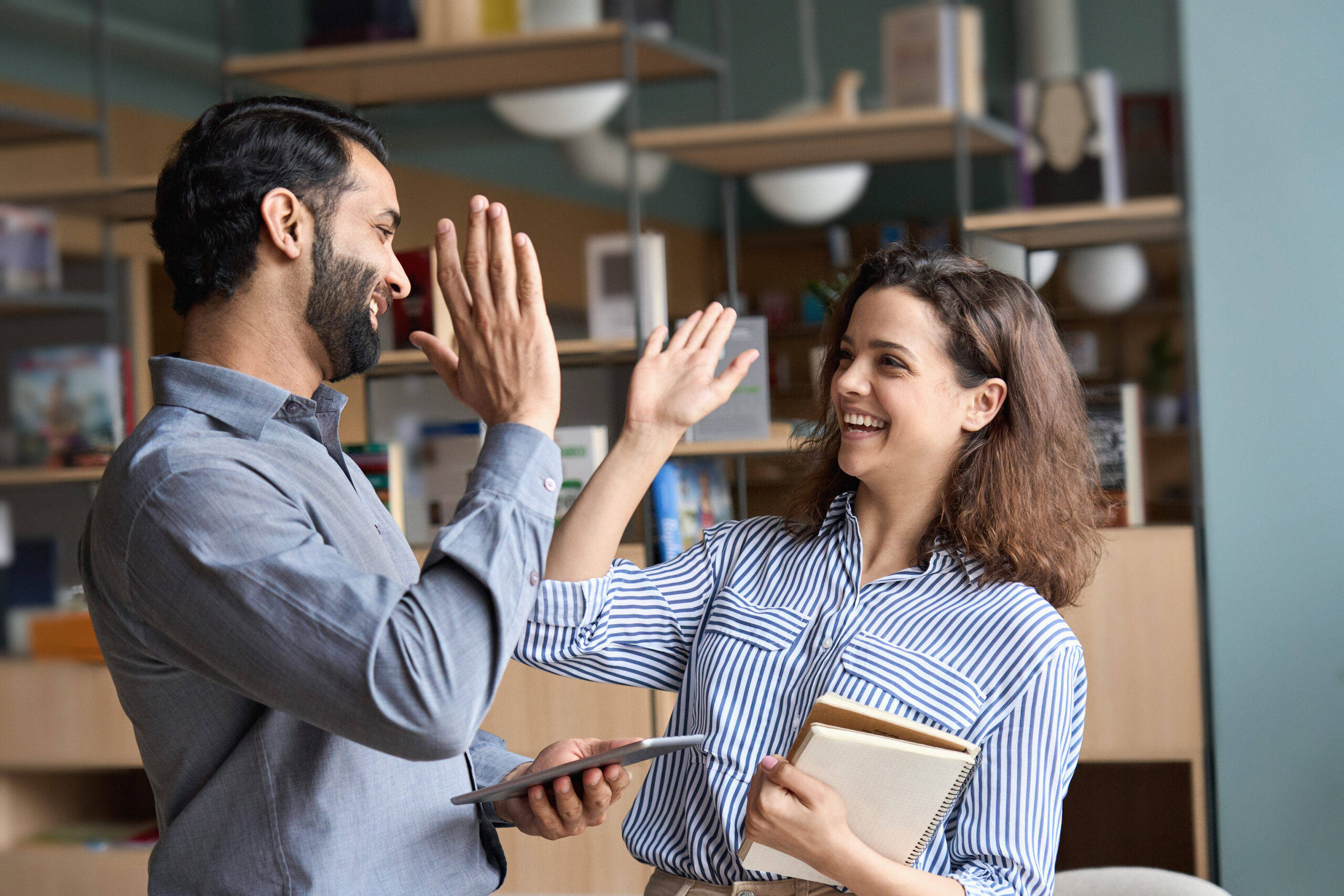 Two happy friendly professionals, teacher and student giving high five standing in office