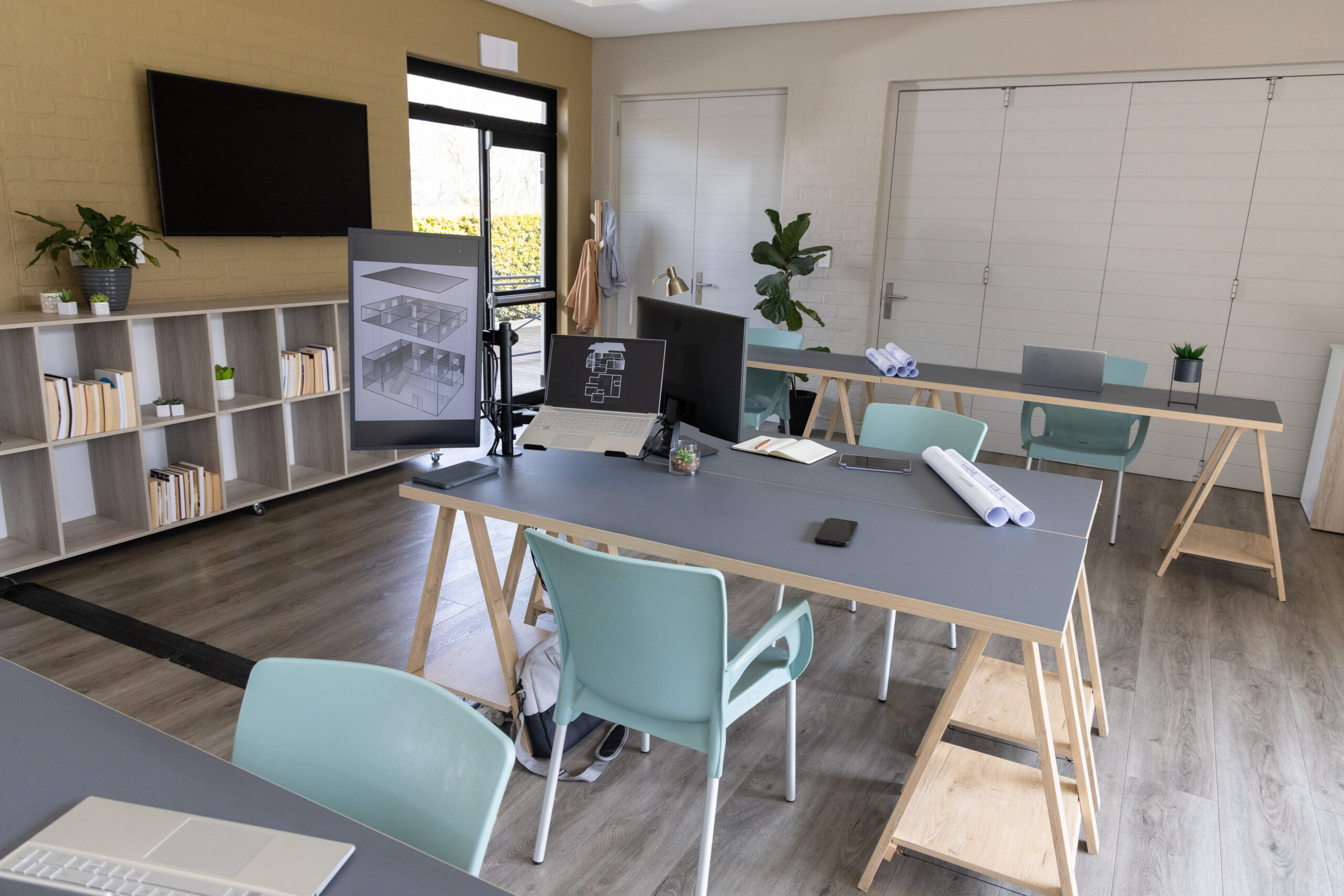 Central trestle desk holding laptop, smartphone and monitor arm displaying floor plans in studio